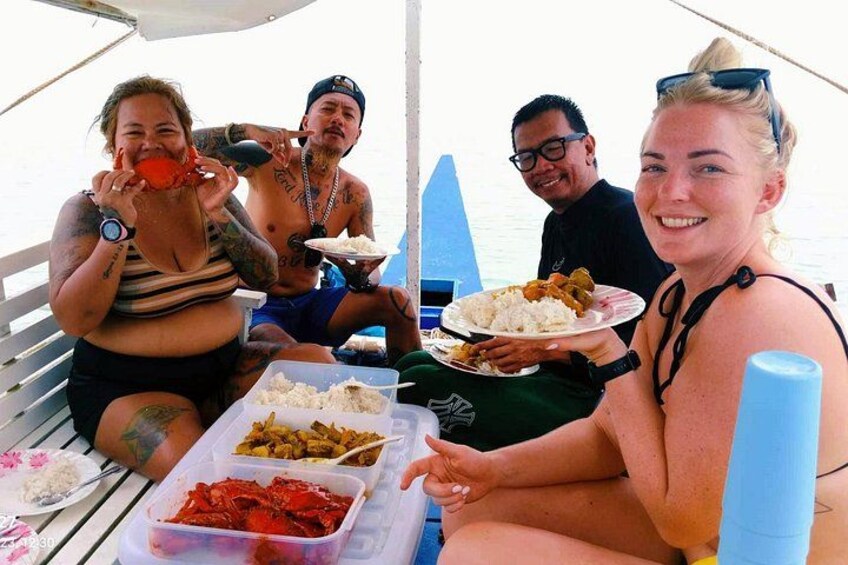 People on a boat eating food, with a table full of dishes and a blue cooler. 3
