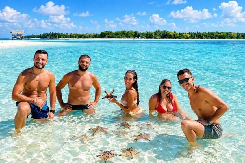 A group of people in clear turquoise water with a beach and palm trees in the background. 1