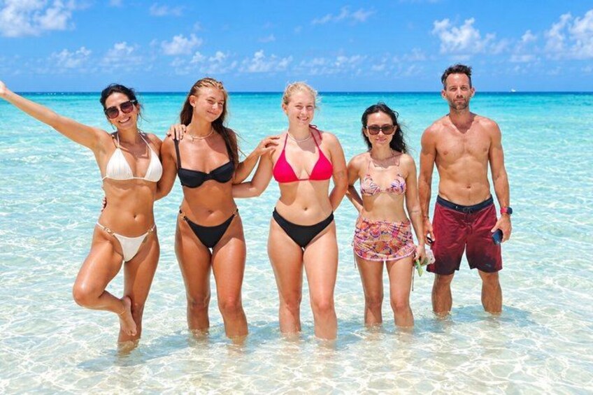 A group of people standing in shallow water on a beach with clear skies. 3