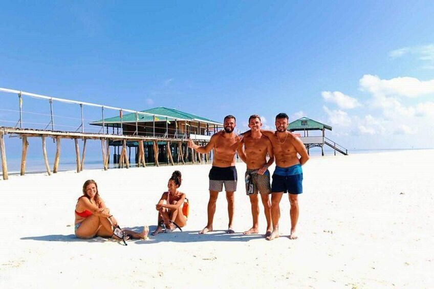 A beach with people, a wooden pier, and a green-roofed structure. 2