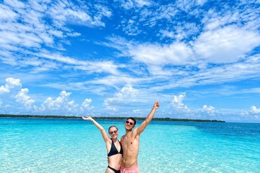 A couple standing in shallow turquoise water with a clear sky and distant land. 5
