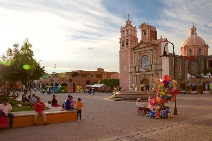 A plaza with a historic church, people sitting on benches, and a fountain with balloons. 4