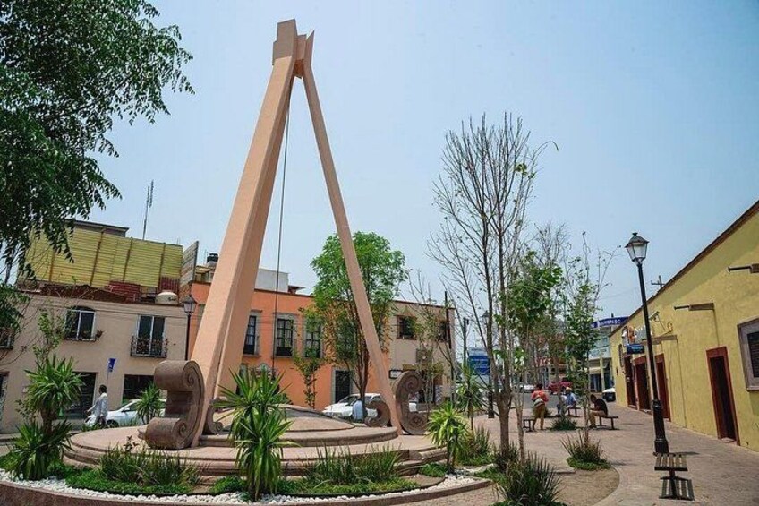 A public square with a large sculpture, palm trees, and buildings. 2