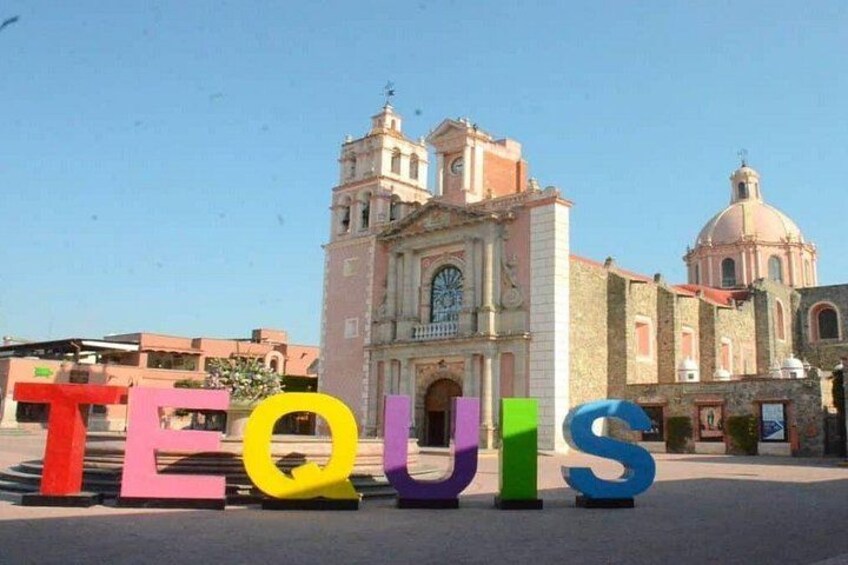 Colorful letters spelling 'TEQUIS' in front of a historic building with a clock tower and dome. 3