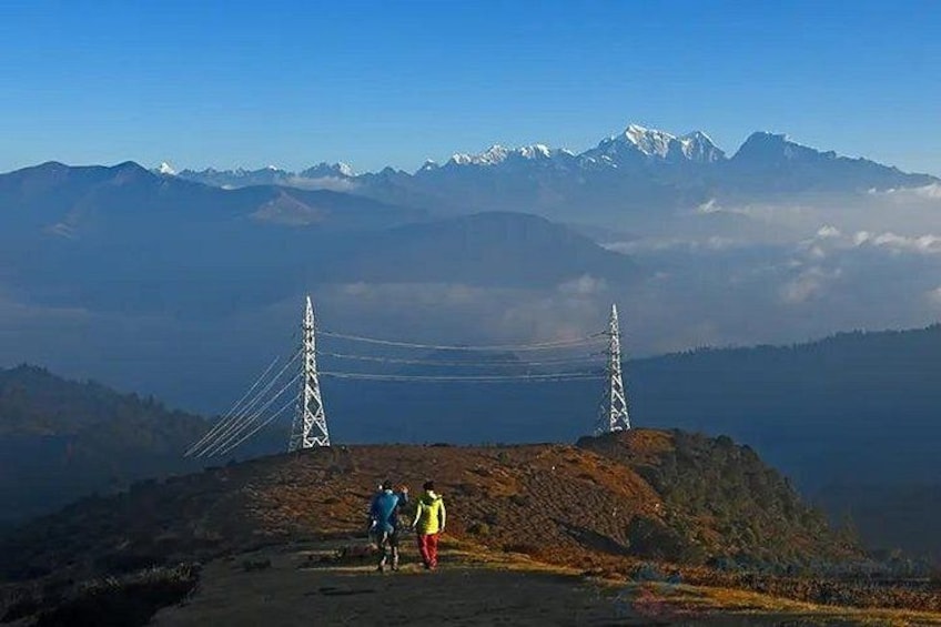 A mountain landscape with two power lines and a bridge, and two people standing on a hill. 1