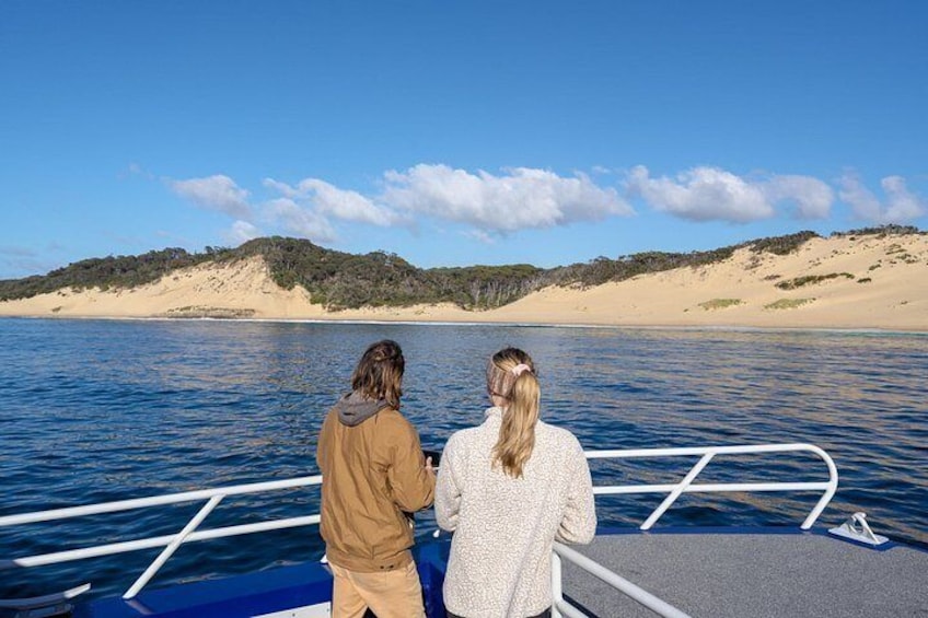Two people on a boat with a sandy beach and hills in the background. 3