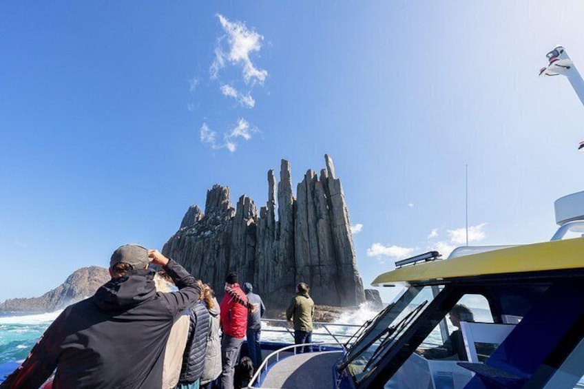 A group of people on a boat near a rocky coastline with tall, narrow rock formations. 2