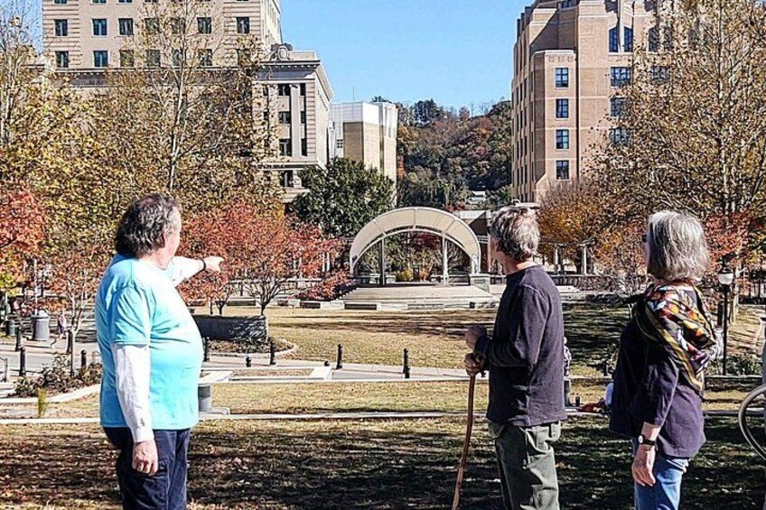 A group of people standing in a park with autumn trees and a large building in the background. 5