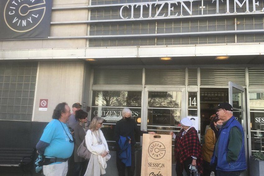 A group of people standing outside a building with a sign that reads 'Citizen Time.' 1