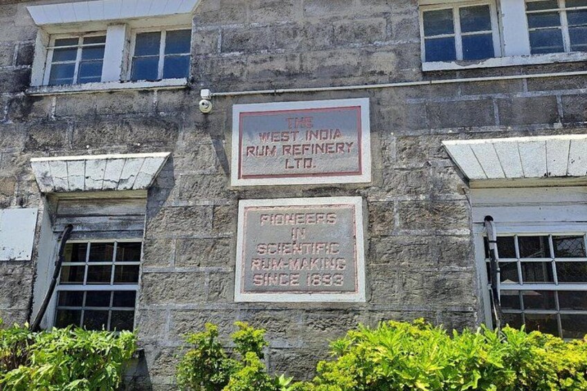 Een gebouw met twee borden. Een bord vermeldt 'The West India Rum Refinery Ltd.' en het andere 'Pioneers in Scientific Rum-Making Since 1893'. 3
