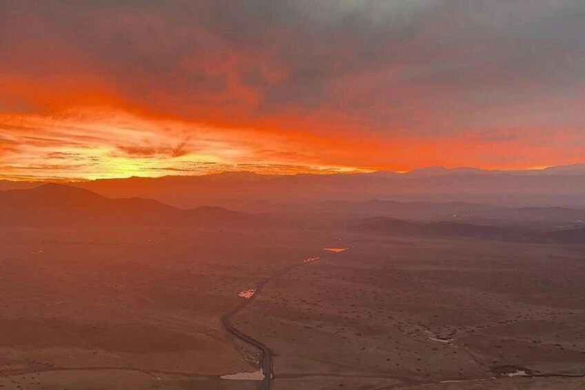 A desert landscape with a winding road and distant mountains under a sunset sky. 2
