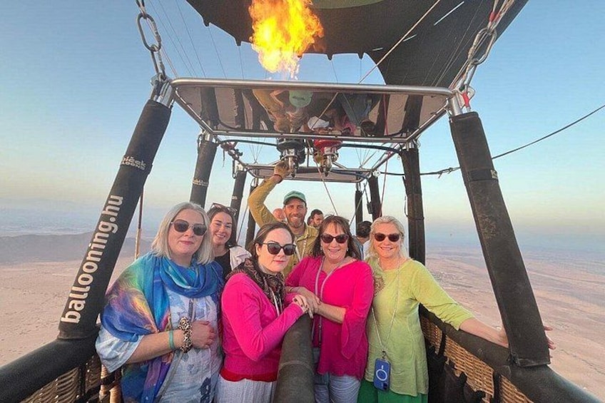 A group of people in a hot air balloon with a fire basket, over a vast, flat landscape. 4