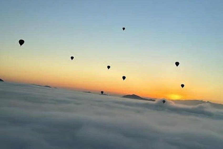 Hot air balloons floating above a sea of clouds at sunrise. 3