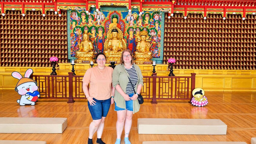 To personer står foran en stor Buddha-statue med et farverigt muralmaleri i baggrunden. 3
