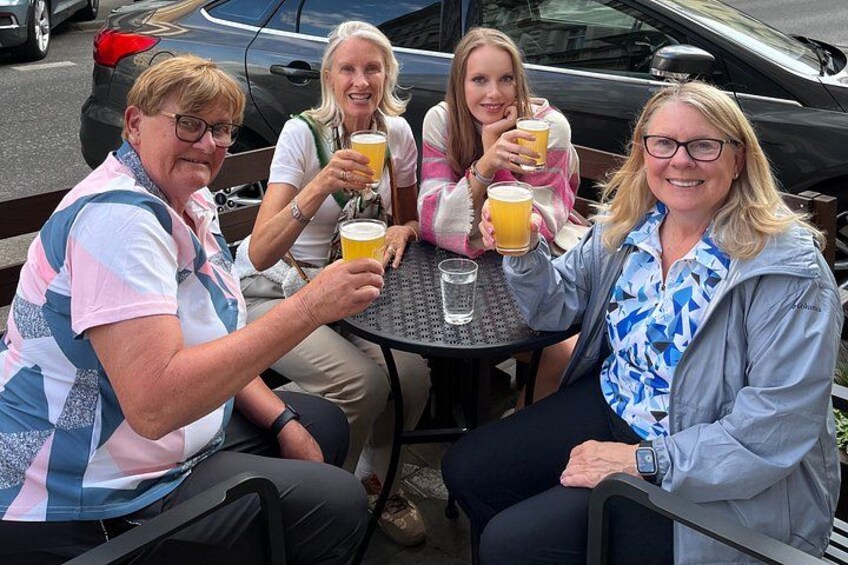 Vier personen zitten buiten aan een ronde tafel, met biertjes. 5