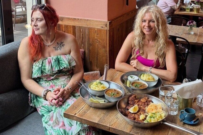 Twee vrouwen zitten aan een tafel met verschillende gerechten ervoor. 3