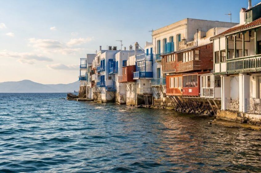 A coastal town with buildings extending into the water, a clear sky, and mountains in the distance. 3