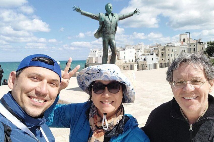 Three people posing in front of a statue and a coastal town. 2