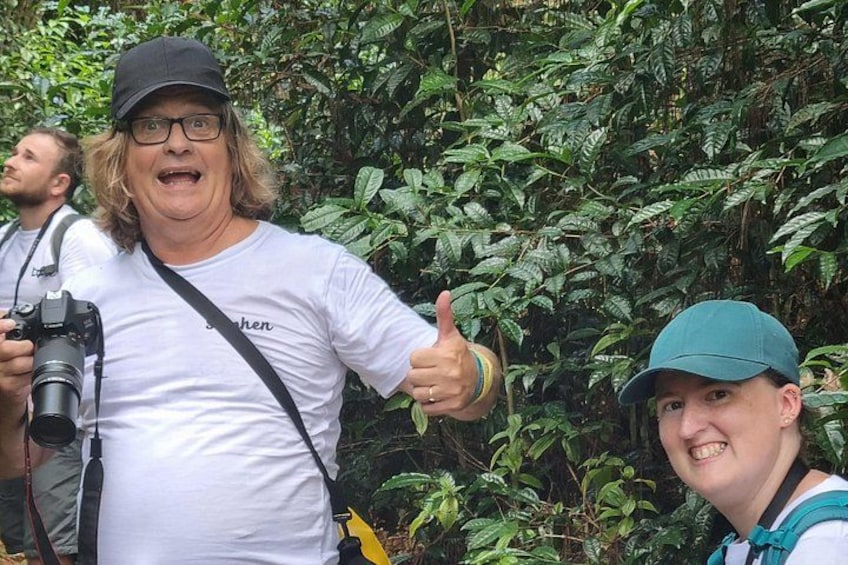 A person with a camera and a thumbs-up gesture, standing in a forested area. 5