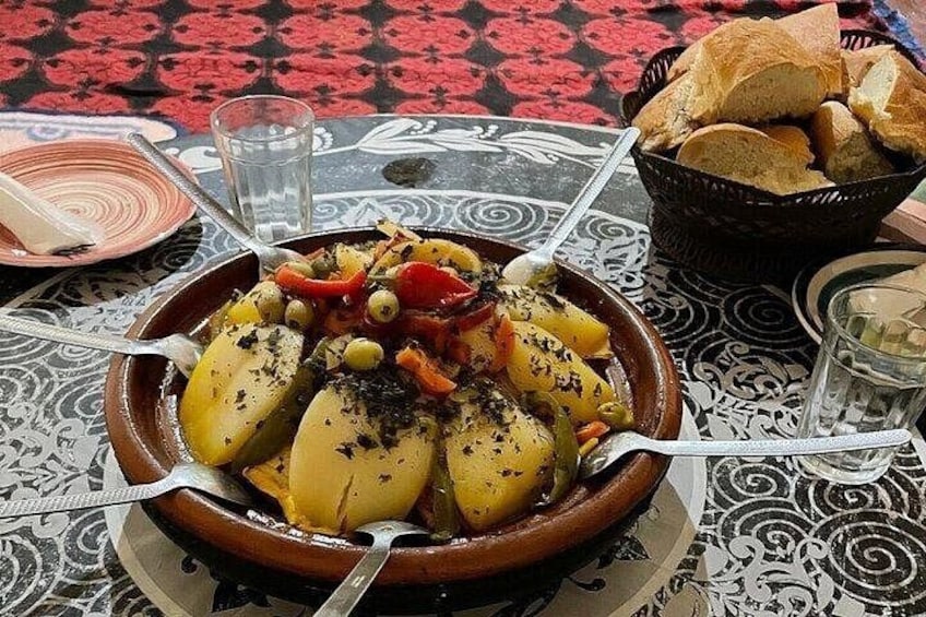 A traditional dish with potatoes, olives, and peppers on a patterned tablecloth. 2
