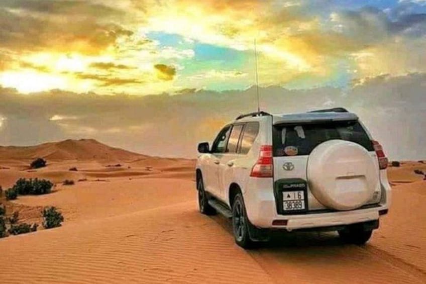 A white SUV parked on a sandy dune with a clear sky and distant mountains. 1