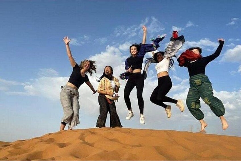 A group of people jumping on a sand dune with a clear sky in the background. 2