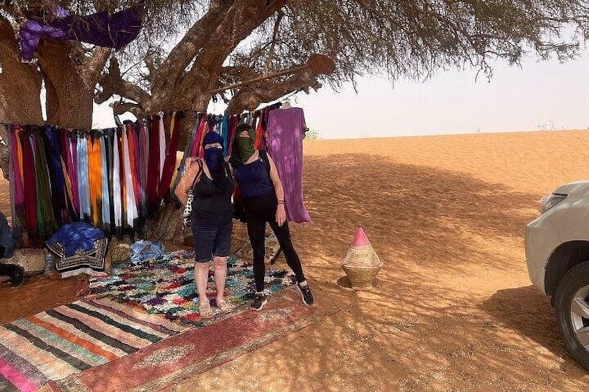 Two people standing under a tree with colorful fabrics hanging nearby. 2
