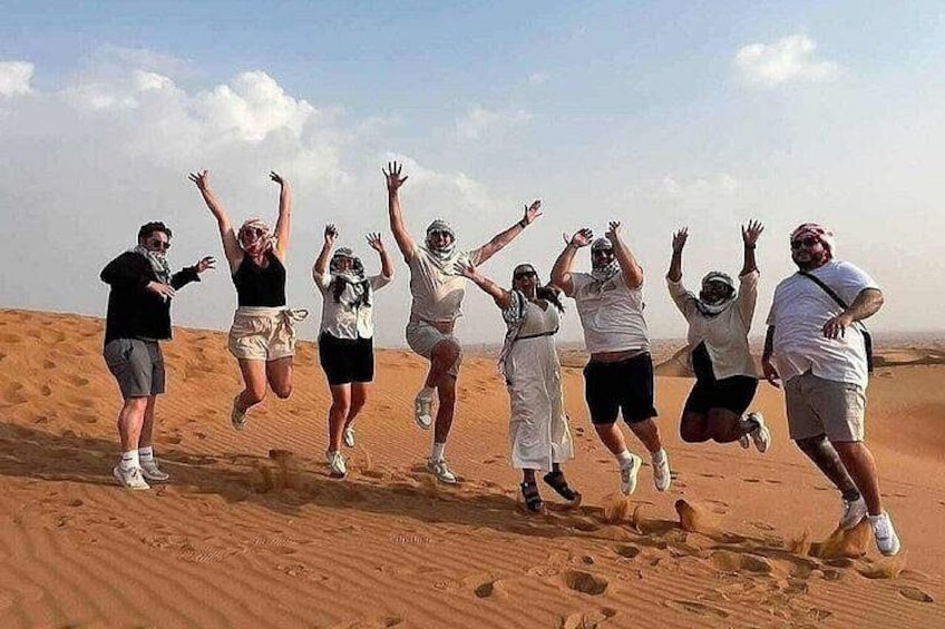Eine Gruppe von Menschen springt in einer Wüste vor einer Landschaft aus Sanddünen. 3