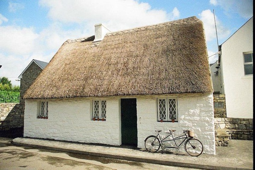 Une maison blanche avec un toit de chaume et un vélo garé devant. 1