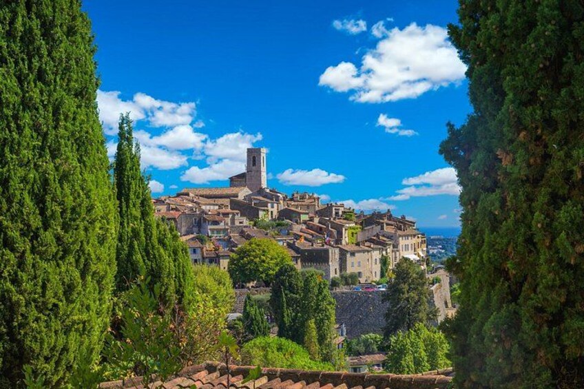 Un pueblo histórico con una torre destacada, rodeado de abundante vegetación y un cielo azul despejado. 1