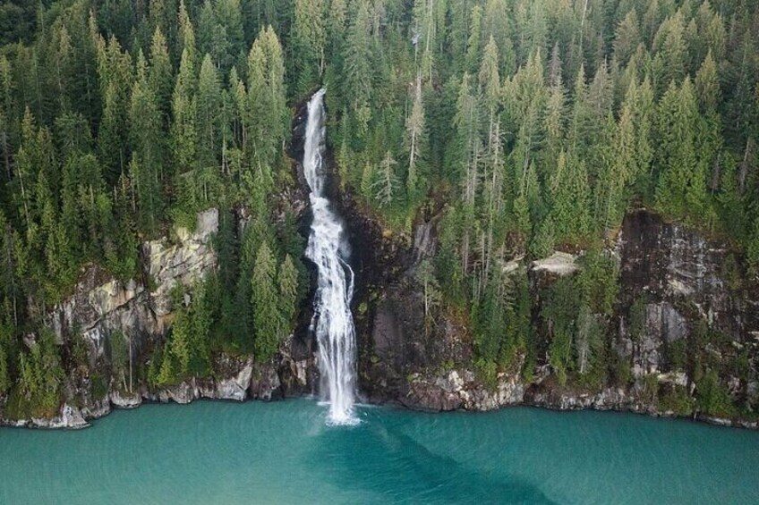 Une cascade se jetant dans un lac turquoise, entouré d’une forêt dense. 5