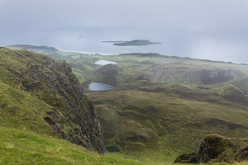 Eine zerklüftete Landschaft mit grünen Hügeln, einem kleinen See und einer entfernten Insel. 2