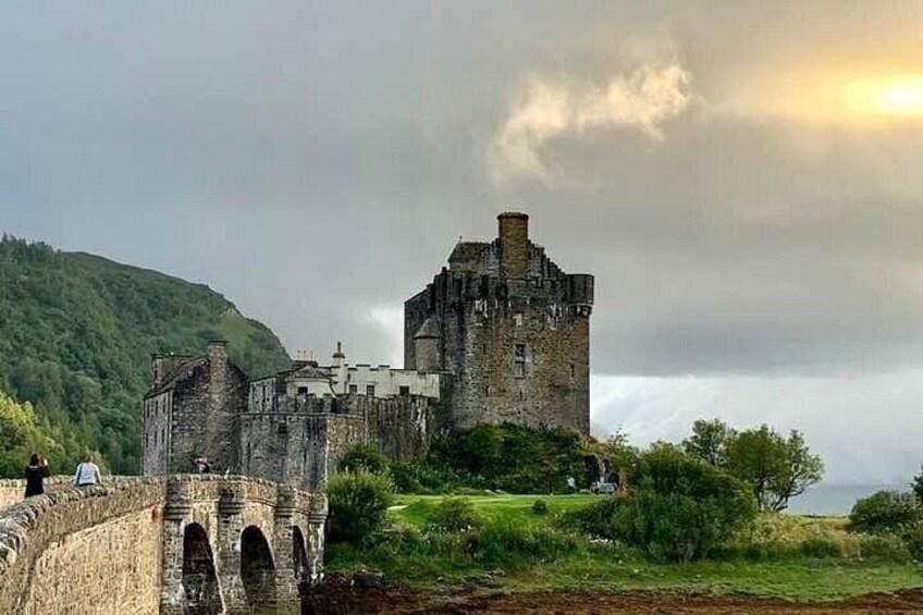 A historic castle on a hill, surrounded by greenery and a stone bridge. 3