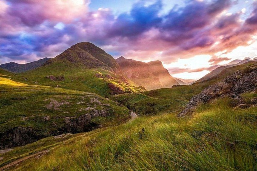 Eine gebirgige Landschaft mit grasbewachsenen Hängen und einem gewundenen Pfad. 1