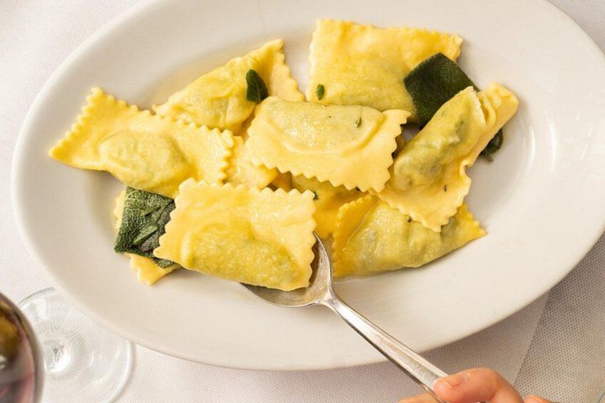 Ein Teller Ravioli mit einer Gabel, ein Weinglas und eine weiße Tischdecke. 3