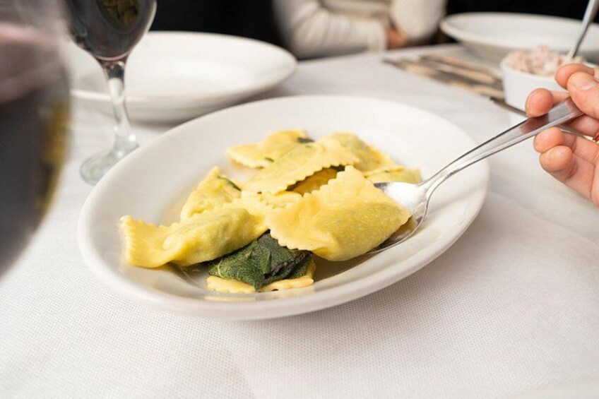 Ein Teller Ravioli, eine Gabel, ein Weinglas und eine Schüssel Soße auf einem Tisch. 2