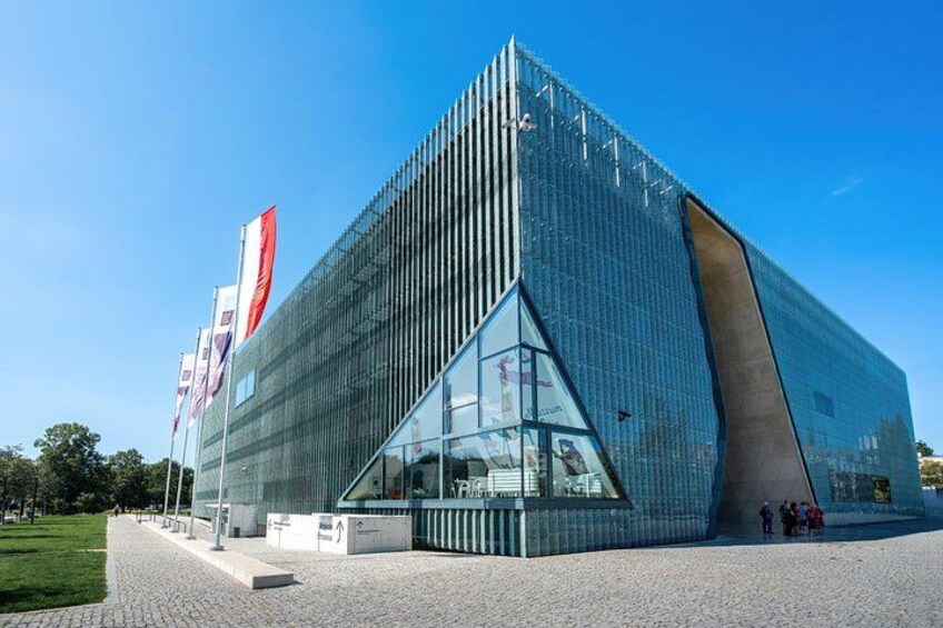 Un bâtiment moderne en verre, doté d’une conception triangulaire originale, entouré d’une zone pavée et de drapeaux. 4