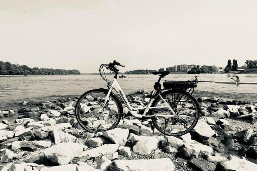 Un vélo est garé sur une plage rocheuse, au bord d’une étendue d’eau, avec une vue sur la ville en arrière-plan. 1