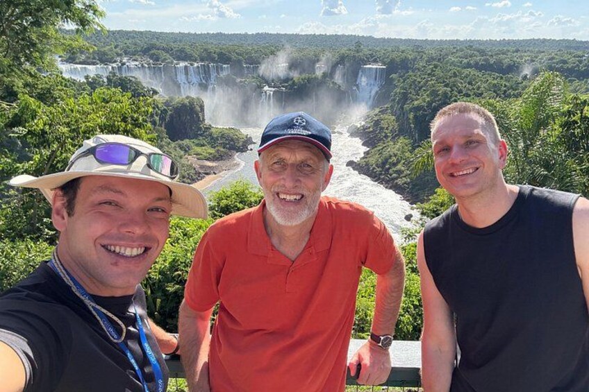 Tres personas de pie junto a una cascada, con abundante vegetación al fondo. 1