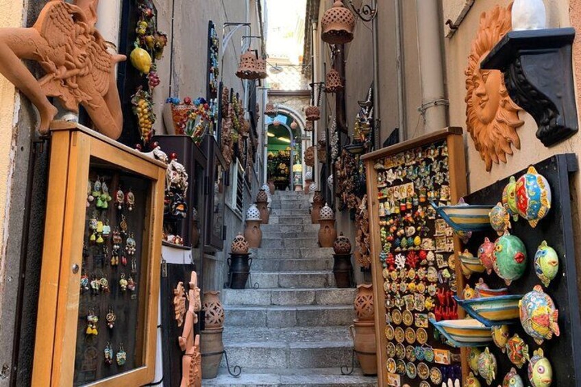 A narrow street with shops on either side, displaying various items like pottery and figurines. 4