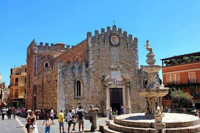 Un edificio de piedra histórico con una torre, una fuente y una multitud de personas. 4