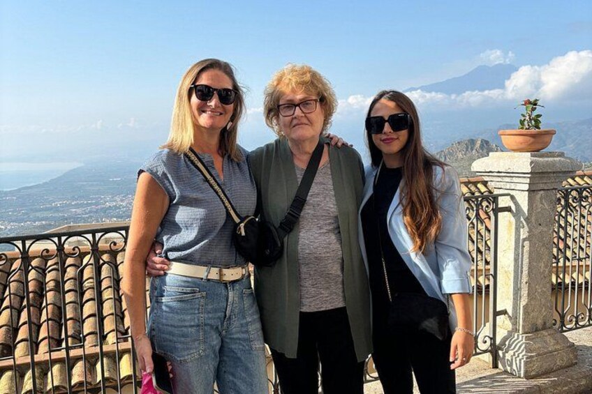 Tres personas en un balcón con vistas panorámicas a una montaña y al mar. 3