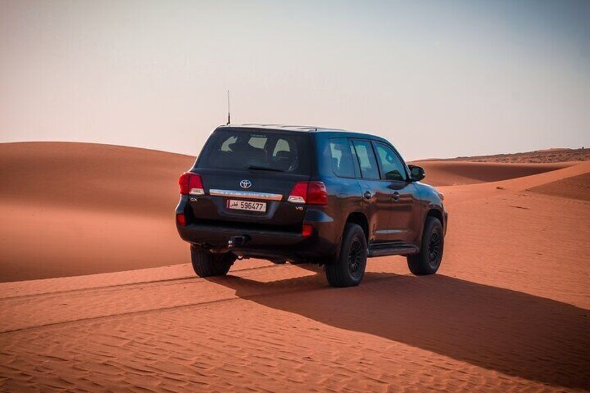 A dark-colored SUV driving on a sandy desert road. 4