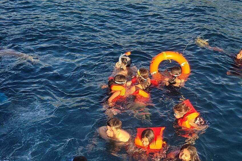 A group of people swimming in the ocean, some wearing life jackets and others in the water. 3