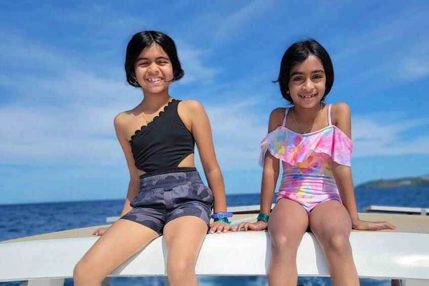 Two individuals sitting on a boat with a clear blue sky and ocean in the background. 4
