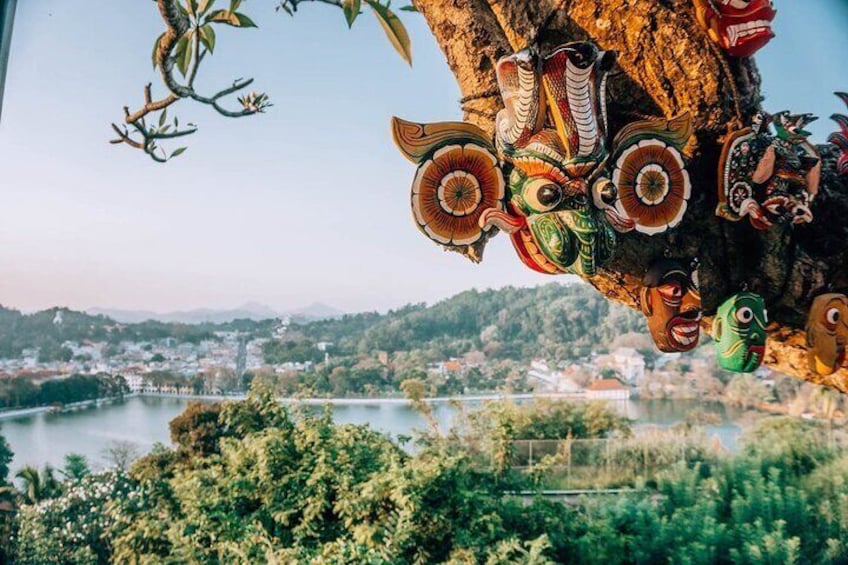 A river with a town in the background, a tree with colorful masks, and a clear sky. 1