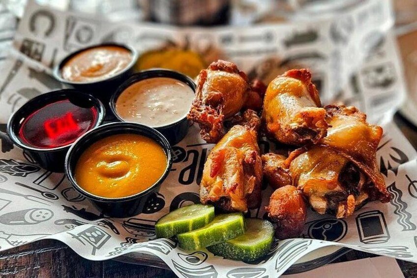 Fried chicken wings with dipping sauces and pickles on a newspaper-lined table. 2