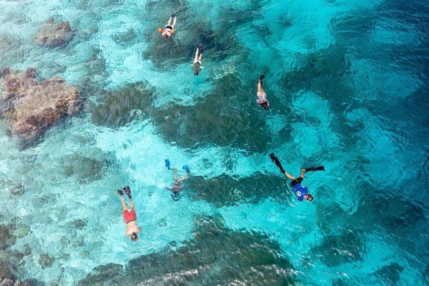 People snorkeling in clear turquoise water with visible rocks. 2