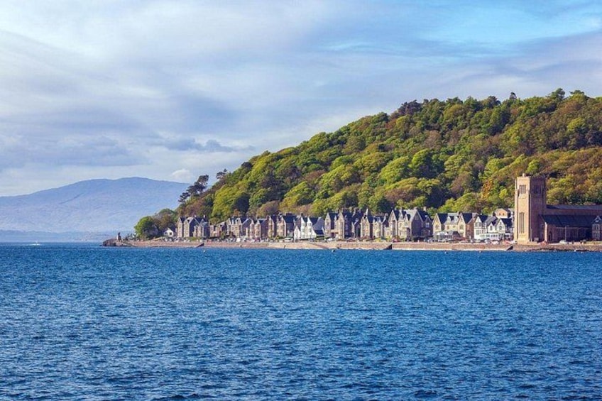 A coastal town with a row of houses along the shore, a church, and a hill with trees. 5