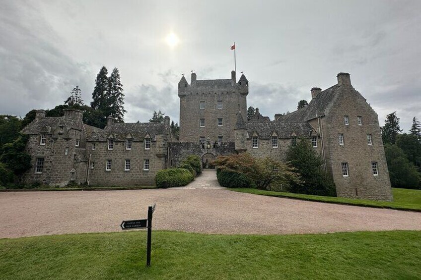 A large stone castle with a flag on top, surrounded by well-maintained lawns and trees. 1
